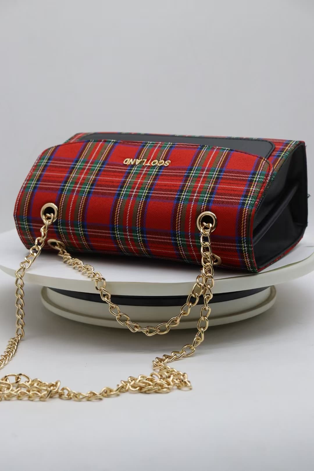 Underside of red tartan crossbody bag showing chain routing and structured base